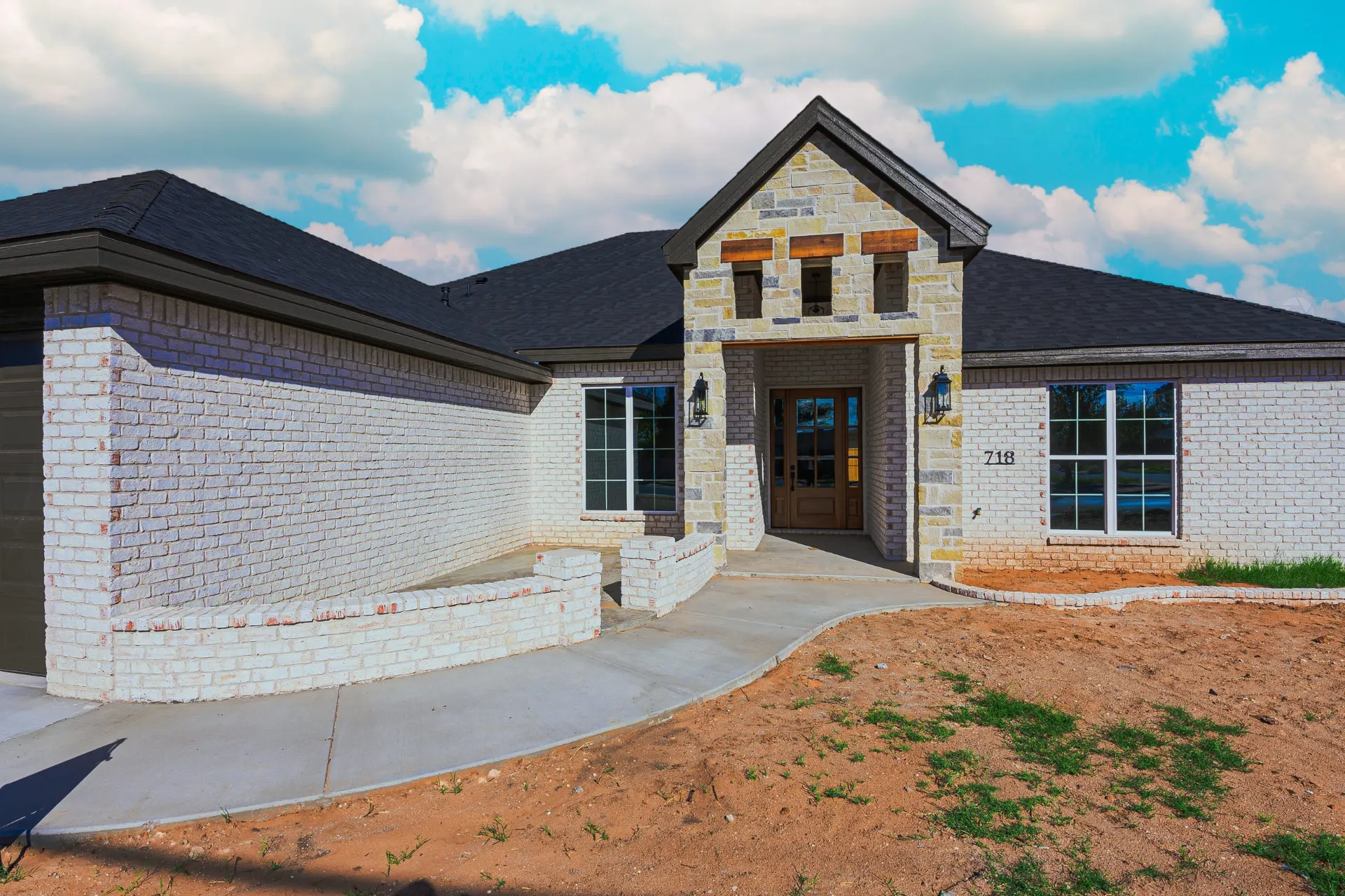 Front elevation of 718 K Ave in whitewashed brick with a multi-tone stone entry gable, natural wood header and a dark wood-and-glass front door